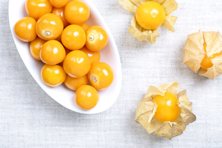 Eine weiße Schale gefüllt mit orangefarbenen Physalis-Früchten neben drei Früchten in ihren getrockneten Kelchen.