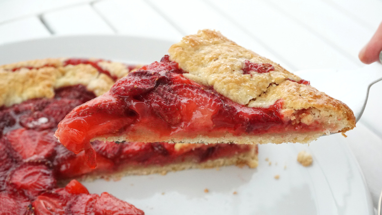 Ein angeschnittenes Stück Erdbeergalette auf einem Tortenheber über einem weißen Teller.