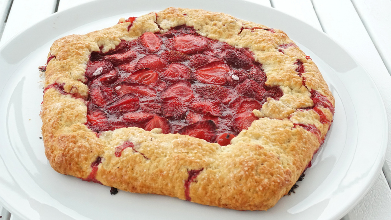 Eine fertig gebackene, runde Erdbeergalette mittig auf einem schlichten weißen Teller platziert.