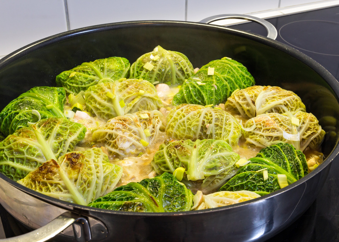 Viele mit Fleisch gefüllte Wirsingwickel schmoren in einer hellen Sauce in einer großen schwarzen Pfanne auf dem Herd.