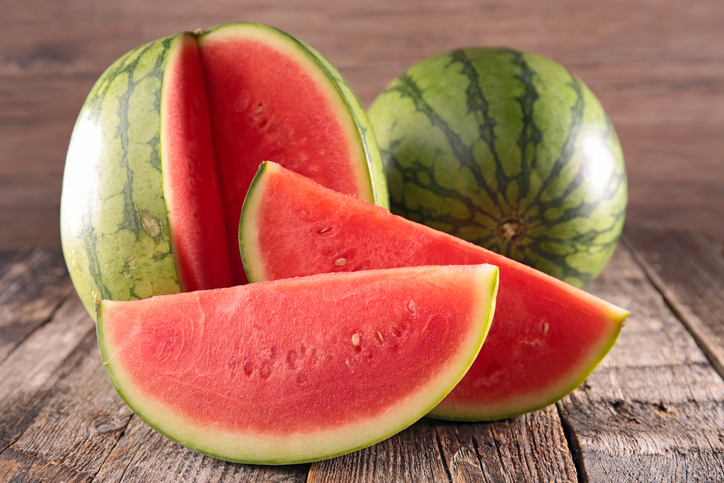 Eine aufgeschnittene Wassermelone mit saftigen Stücken liegt auf einem rustikalen Holztisch.