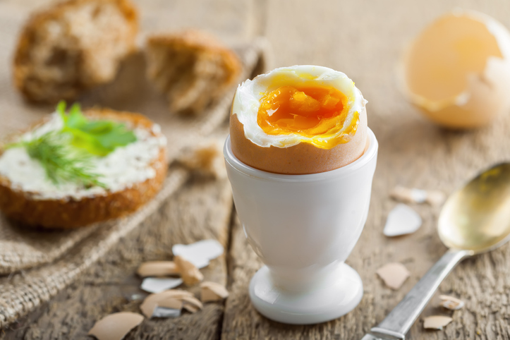 Ein weichgekochtes Hühnerei in einem weißen Eierbecher steht neben einem Stück Brot.