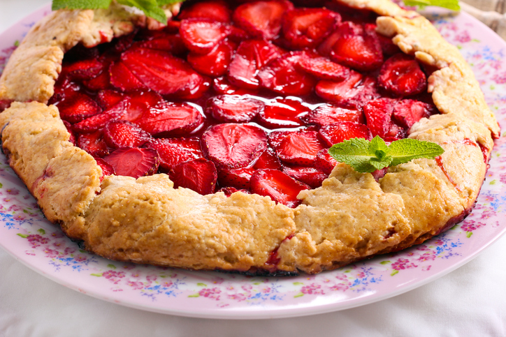 Eine ganze Erdbeergalette auf einem floral gemusterten Teller, garniert mit frischen Minzblättern.