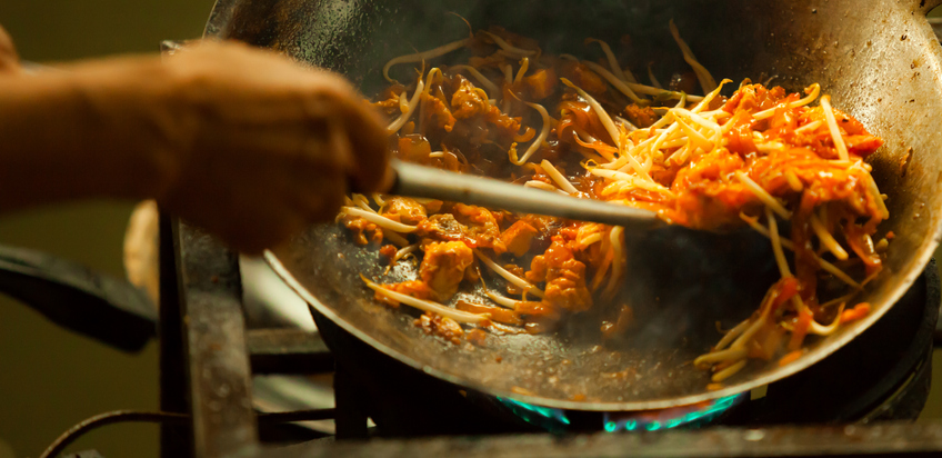 Ein Koch rührt Pad Thai in einer heißen Wok-Pfanne um, während Dampf aufsteigt