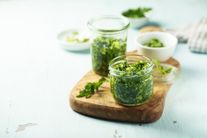 Mehrere Gläser mit frisch zubereitetem grünen Bärlauchpesto stehen auf einem Holzbrett.