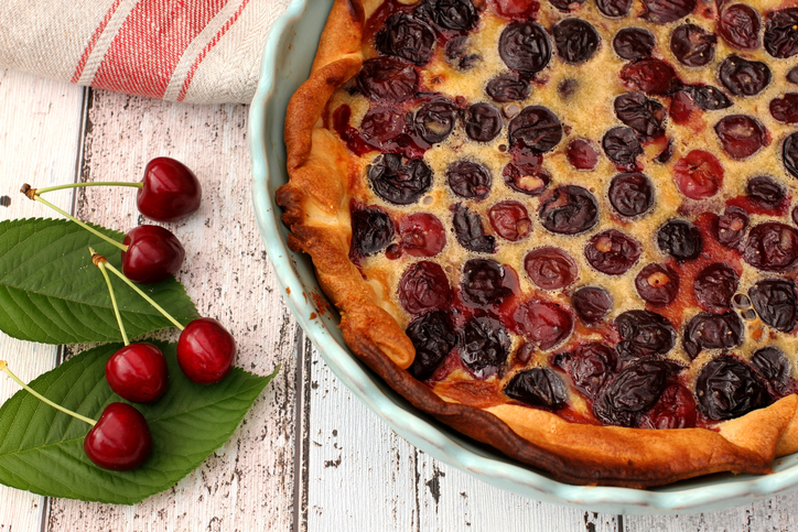 Eine hausgemachte Clafoutis mit vielen Kirschen in einer hellblauen Backform.