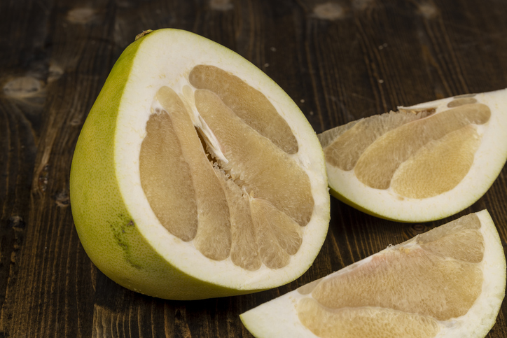 Eine aufgeschnittene Pomelo liegt neben zwei herausgelösten Segmenten auf einer dunklen Holzoberfläche.