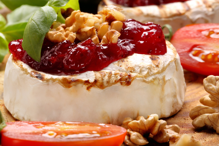 Ein einzelner gegrillter Camembert, reichlich belegt mit Preiselbeerkonfitüre und Walnusskernen.