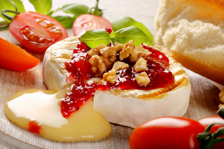 Ein gebackener Camembert mit Preiselbeeren und Walnüssen, aus dem der warme Kern cremig herausfließt.