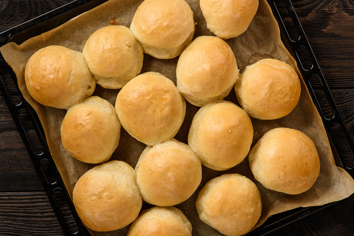 Zahlreiche frisch gebackene, runde Kartoffelbötchen liegen auf einem Backblech mit Backpapier.