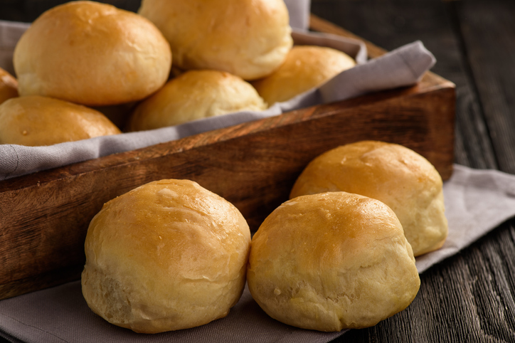Goldbraune, frisch gebackene Kartoffelbötchen liegen in einer rustikalen Holzkiste auf einem grauen Tuch.