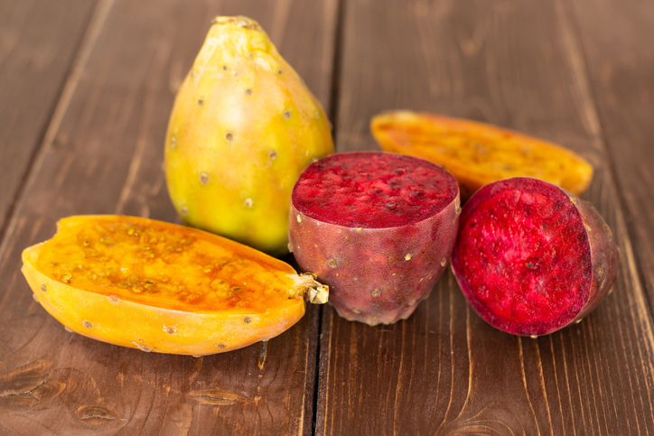 Gelbe und rote Kaktusfeigen ganz und aufgeschnitten auf einem Holztisch
