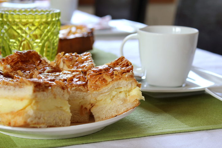 Stücke vom Bienenstich mit cremiger Füllung und karamellisierten Mandeln neben einer Tasse Kaffee
