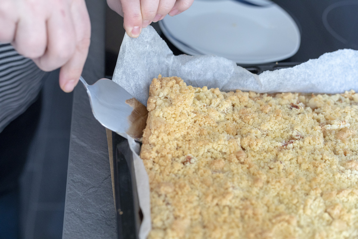 Ein Apfelstreuselkuchen mit goldbraunen Streuseln liegt auf Backpapier in einer Form.