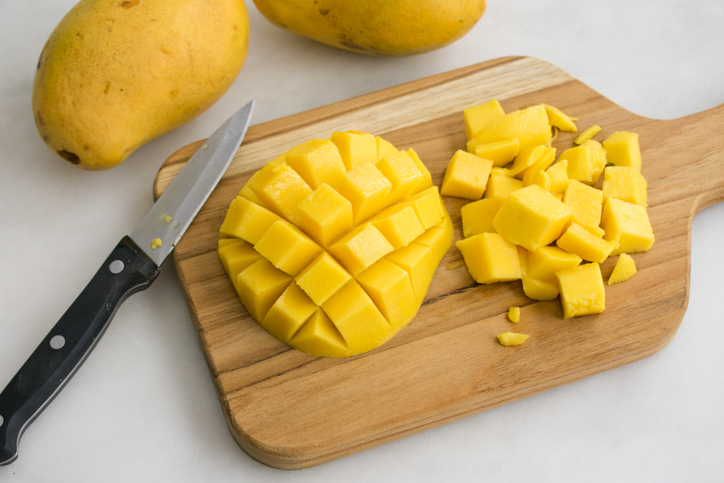 Aufgeschnittene Mango mit Fruchtwürfeln auf einem Holzbrett neben einem Messer