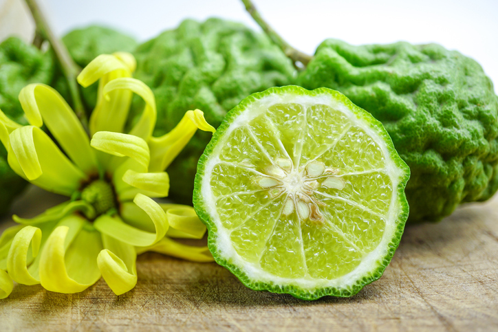 Eine aufgeschnittene Bergamotte liegt mit grüner Schale, Fruchtfleisch und gelber Blüte auf Holz.