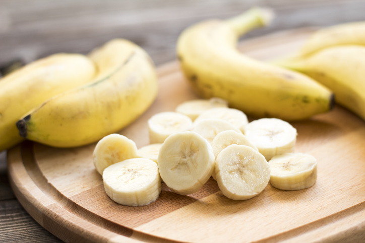 Reife Bananen und geschnittene Bananenscheiben auf einem Holzbrett in heller Nahaufnahme.