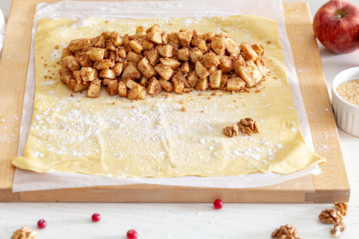 Strudelteig wird mit gewürfelten Äpfeln, Zimt, Zucker und Walnüssen für Apfelstrudel belegt.