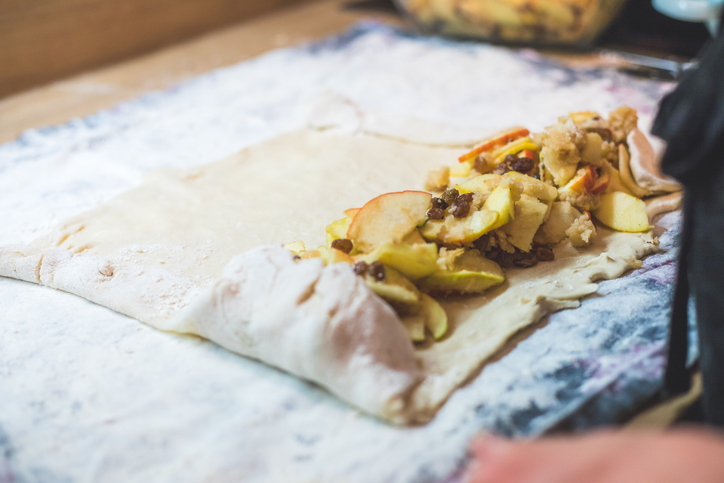 Dünner Strudelteig wird mit Äpfeln, Rosinen und Bröseln gefüllt und vorsichtig eingerollt.