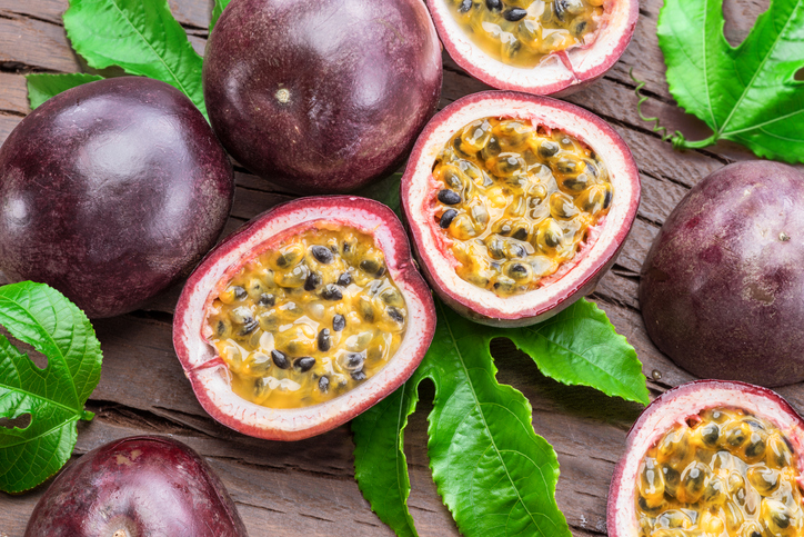 Aufgeschnittene Maracujas mit gelbem Fruchtfleisch und schwarzen Kernen liegen auf grünen Blättern.