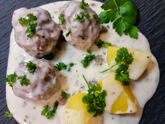 Königsberger Klopse werden mit cremiger Kapernsauce, Kartoffeln und frischer Petersilie serviert.