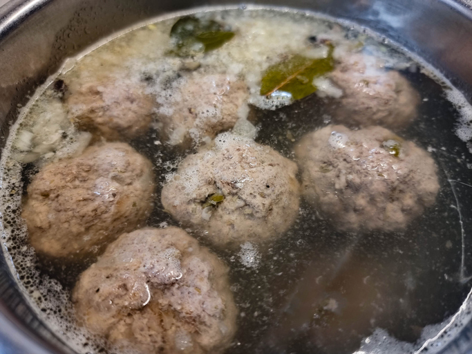 Königsberger Klopse garen in einem Topf mit Brühe, Lorbeerblättern und Gewürzen.