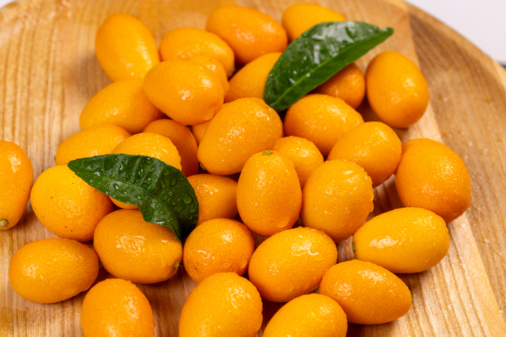 Frisch gewaschene Kumquats mit grünen Blättern auf einem Holzbrett
