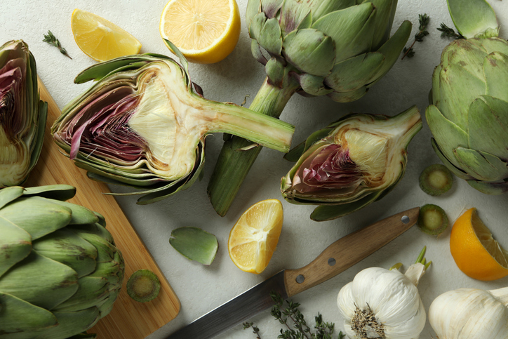 Ganze und halbierte Artischocken mit Zitrone, Knoblauch und Küchenmesser
