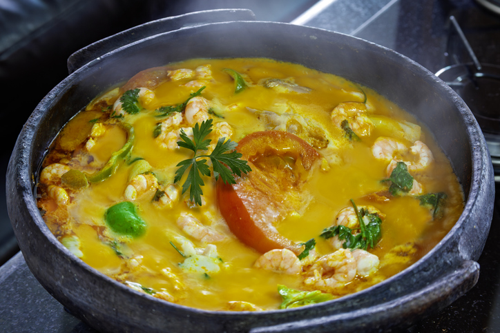 Heiße Moqueca mit Fisch, Garnelen, Paprika und Kräutern in einem schwarzen Topf