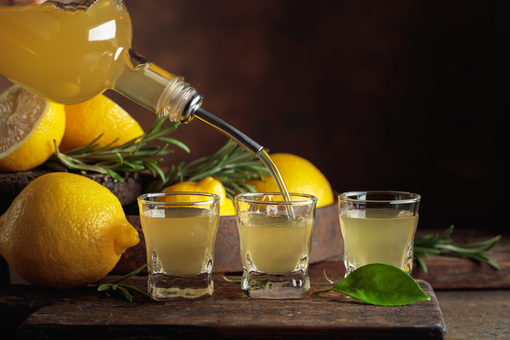 Gelber Limoncello wird aus einer Flasche in kleine Gläser neben frischen Zitronen gegossen.