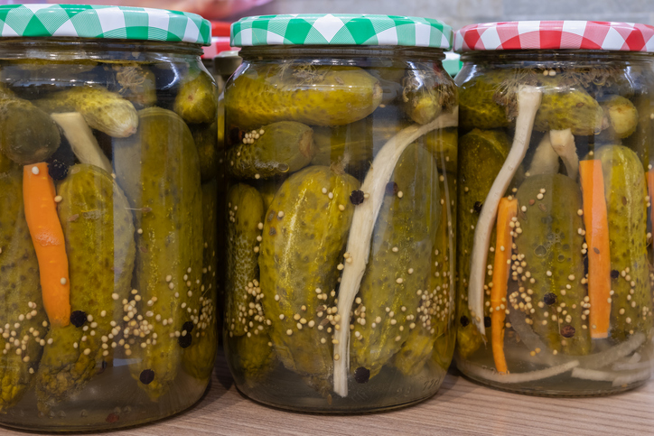 Eingelegte Gurken mit Zwiebeln, Möhren und Gewürzen in verschlossenen Gläsern