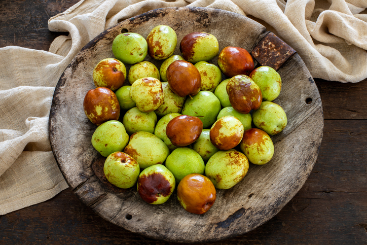 Grüne und braune Jujube-Früchte in einer rustikalen Holzschale
