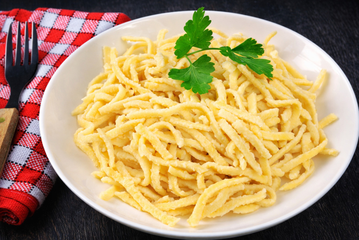 Frische Spätzle liegen in einer weißen Schale und sind mit Petersilie garniert.