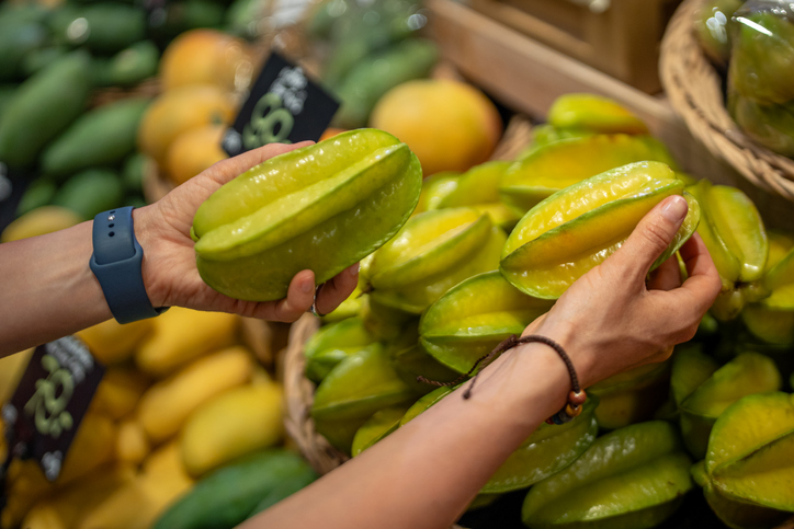 Hände halten grüne und gelbliche Karambole-Früchte an einem Marktstand