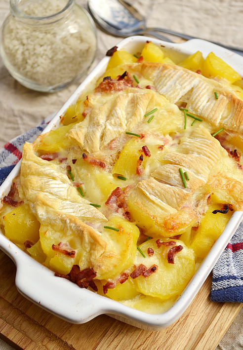 Cremige Tartiflette mit Kartoffeln, Speck und geschmolzenem Käse in einer weißen Auflaufform.