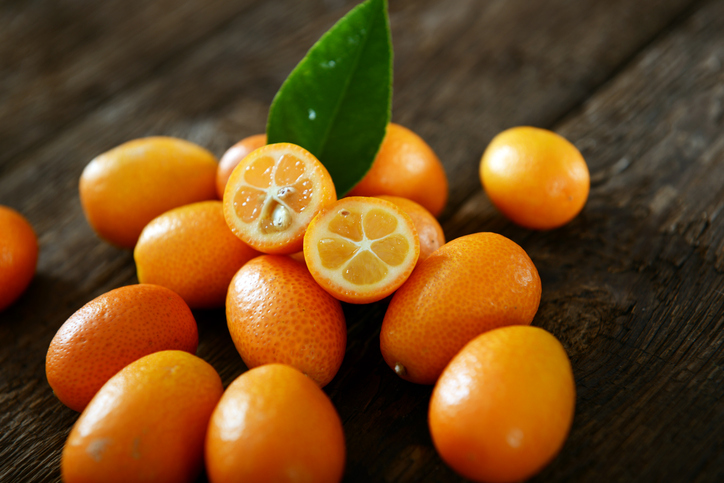 Ganze und halbierte Kumquats mit grünem Blatt auf einem Holztisch