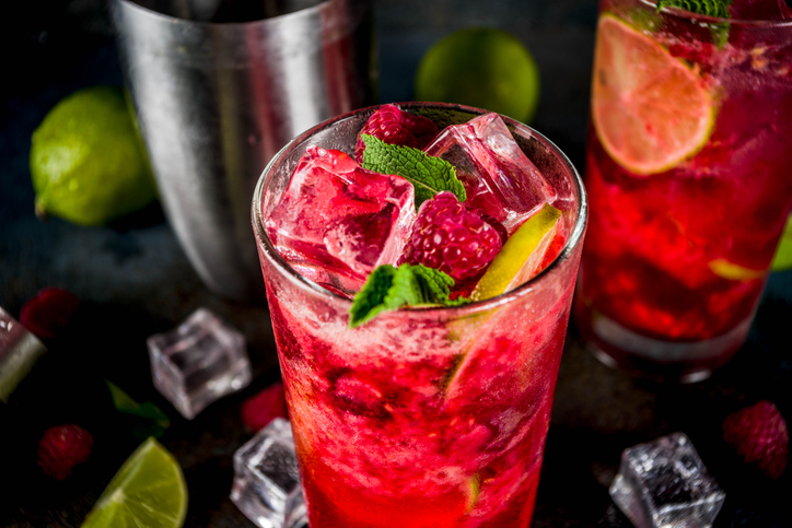 Ein roter Himbeer-Mojito mit Eiswürfeln, Himbeeren, Limette und frischer Minze im Glas.