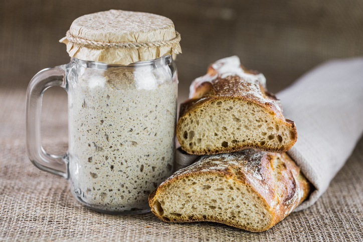 Aktiver Sauerteigansatz in einem Glas neben angeschnittenem Sauerteigbrot mit luftiger Krume.