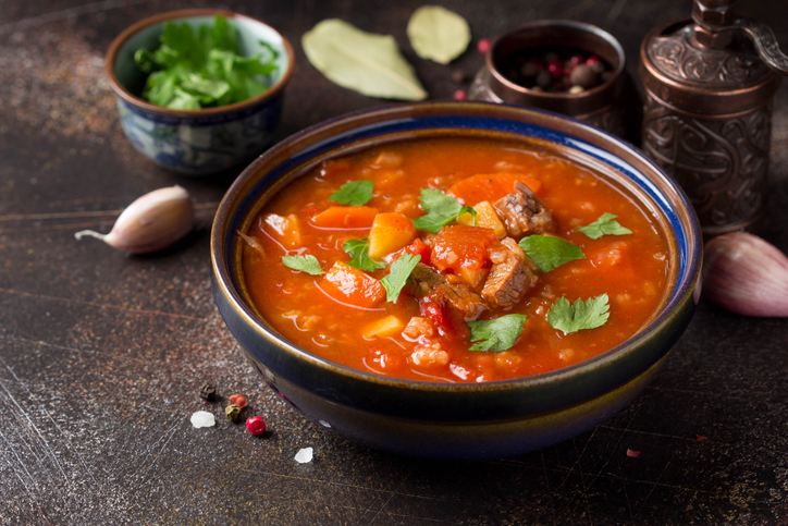 Gulaschsuppe in einer dunklen Schale mit Fleisch, Gemüse, Kräutern und kräftig roter Brühe auf dunklem Untergrund.