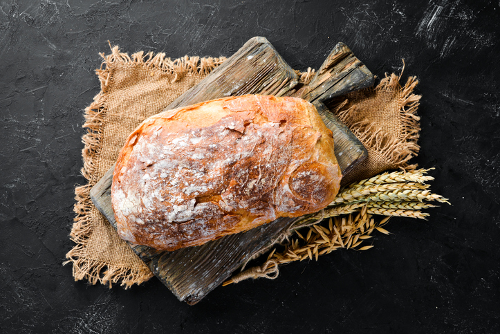 Rustikales Ciabatta mit kräftig gebräunter und bemehlter Kruste auf Holzbrettern neben reifen Weizenähren.