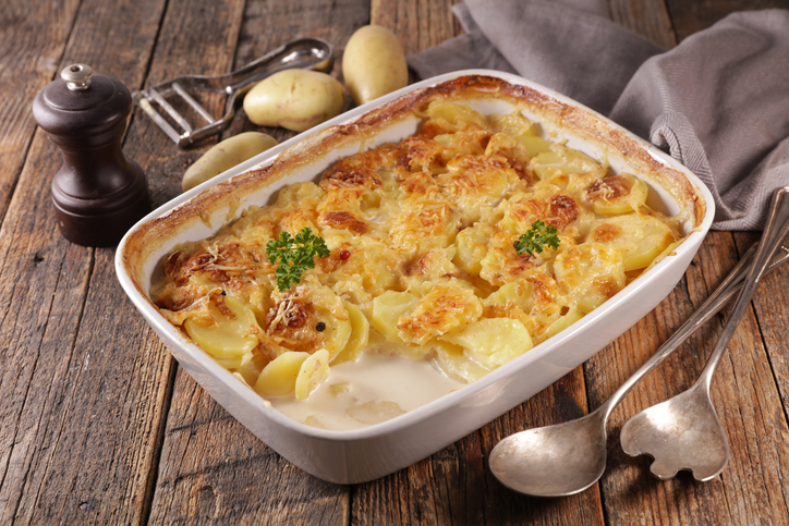 Kartoffel-Gratin in einer rechteckigen weißen Auflaufform mit gebräunter Käsekruste und sichtbaren Kartoffelscheiben auf einem rustikalen Holztisch.