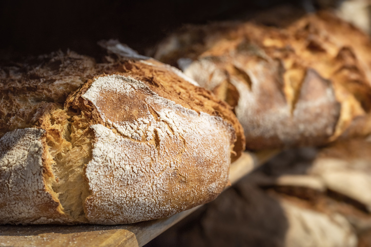 Frisch gebackene Sauerteigbrote mit kräftig gebräunter, bemehlter Kruste auf einem Holzbrett.