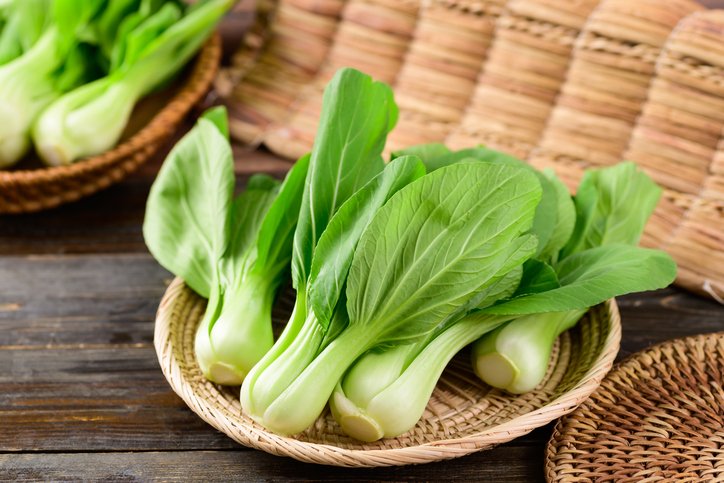 Mehrere kleine Pak-Choi-Köpfe liegen in einer flachen Schale auf einem Holztisch