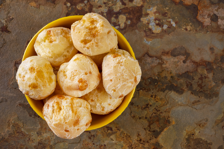 Mehrere runde Pão de Queijo in einer gelben Schale auf einer rustikalen Steinoberfläche.