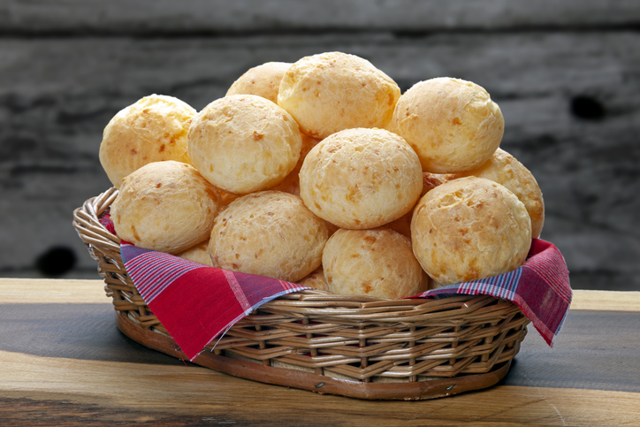 Ein Korb voller Pão de Queijo steht auf einem Tisch, die kleinen brasilianischen Käsebrötchen sind goldgelb gebacken.
