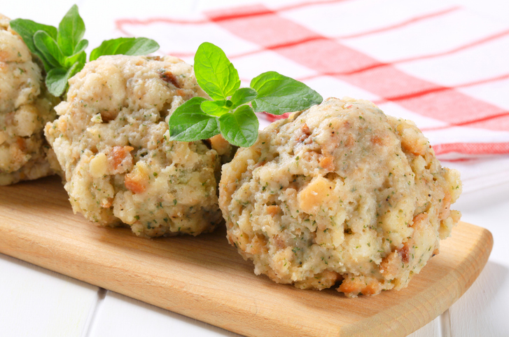 Geformte Semmelknödel liegen auf einem Holzbrett und sind mit Kräutern garniert.