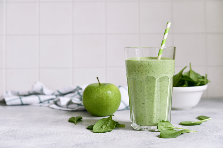 Grüner Apfel-Spinat-Smoothie im Glas mit Trinkhalm, frischem Apfel und Spinatblättern auf einer hellen Küchenfläche