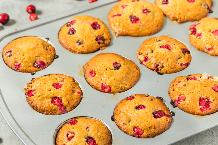 Mehrere goldbraune Cranberry Muffins mit sichtbaren roten Beeren in einer Muffinform direkt nach dem Backen.