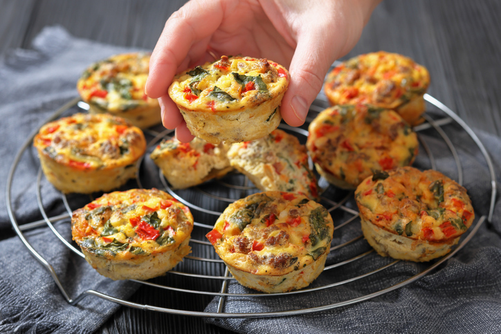 Hand greift nach einem Frittata Eier-Muffin auf einem Gitter mit mehreren gebackenen Eier-Muffins.