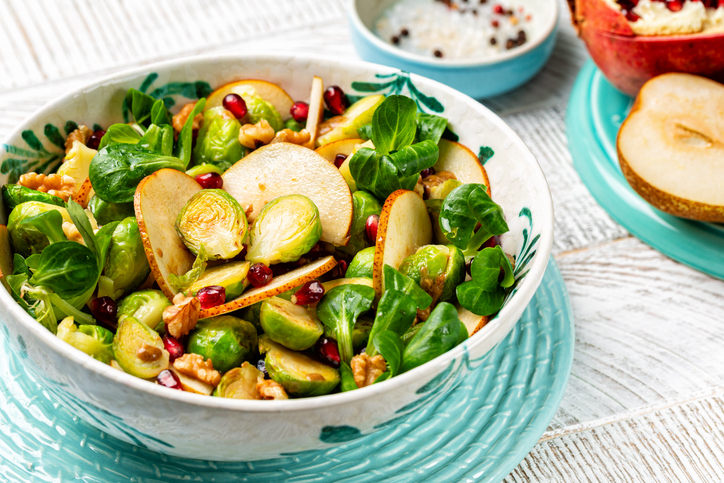 Rosenkohlsalat mit halbiertem Rosenkohl, Birnenscheiben, Feldsalat, Granatapfelkernen und Walnüssen in einer Schale.